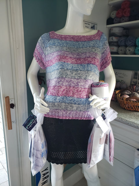 white mannequin wearing sweater and skirt holding organza bags of yarn
