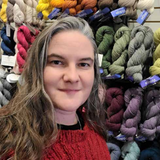 Woman standing in front of a display of colorful yarns in a store.