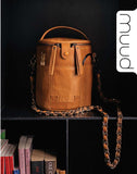 Brown leather bag with chain detail on a dark surface, featuring the brand 'muud'.